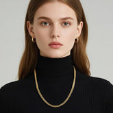 Woman wearing a 14K gold Cuban link chain necklace with chunky, engraved links and a black turtleneck