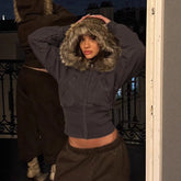 Woman wearing a cropped dark zip-up hoodie with faux fur hood and loose brown joggers.