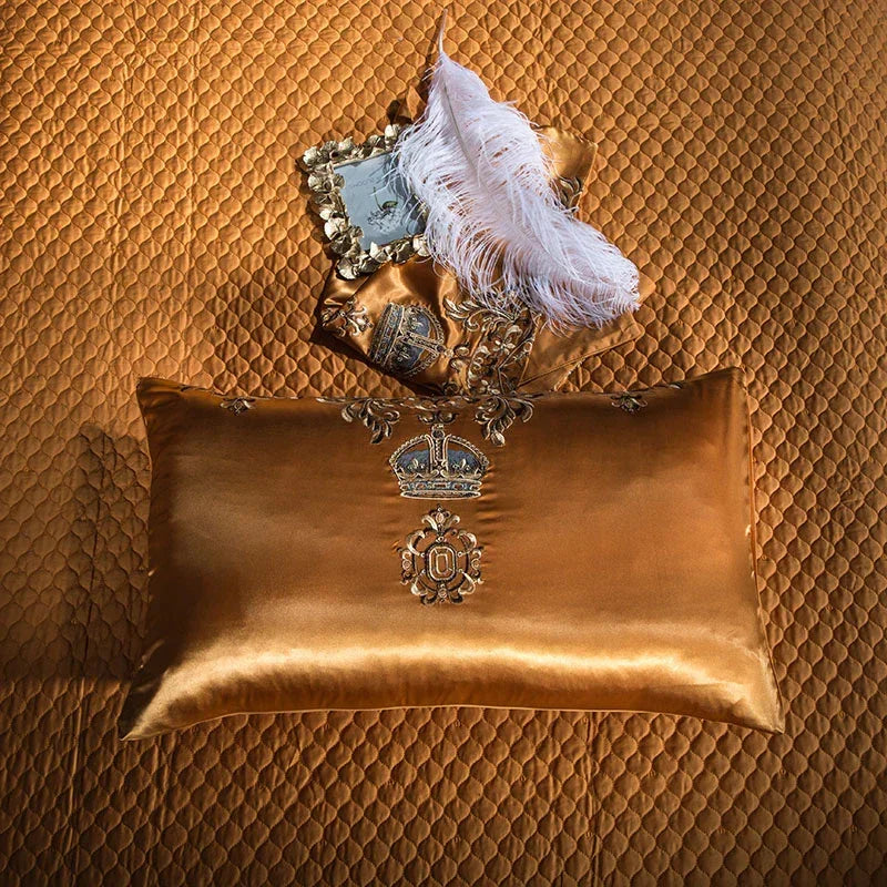 Gold satin pillow with crown embroidery on a quilted gold bedspread, baroque decor accent