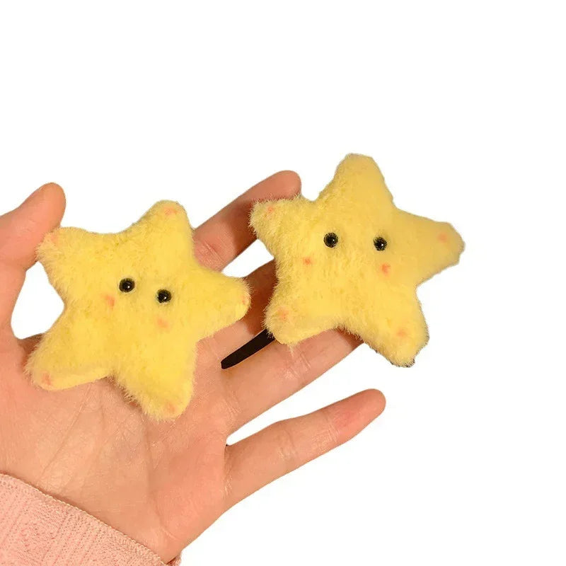 Hand holding two yellow plush star hair clips with cute black eyes and soft texture