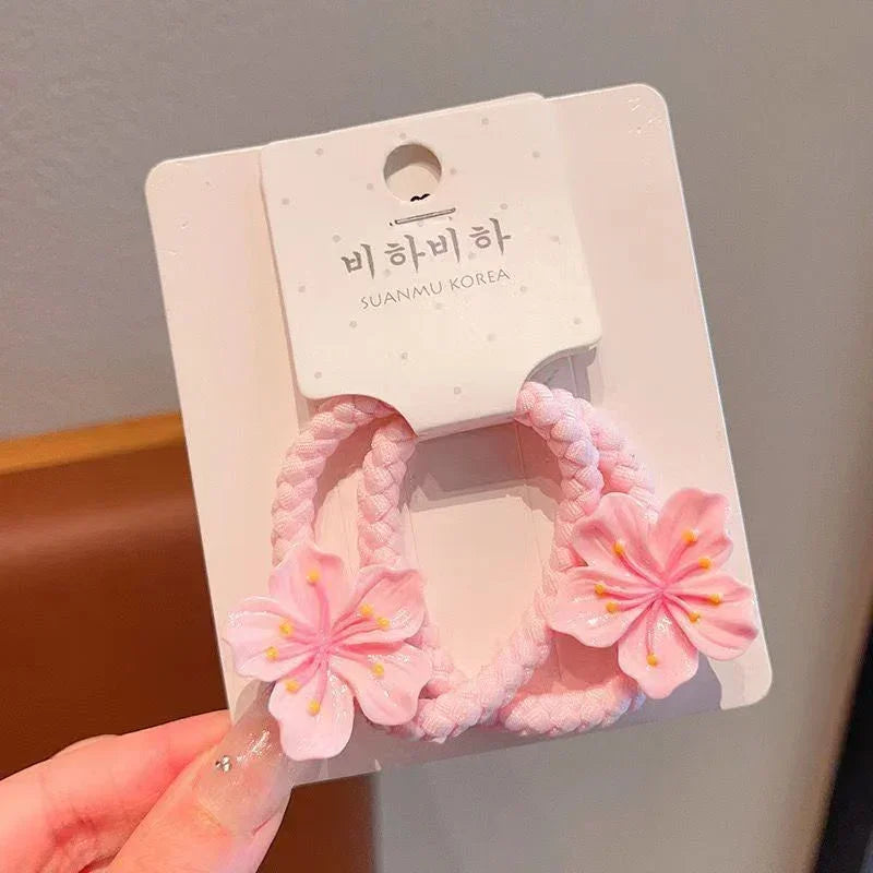 Pair of pink braided hair ties with pink cherry blossom flower accents on display card