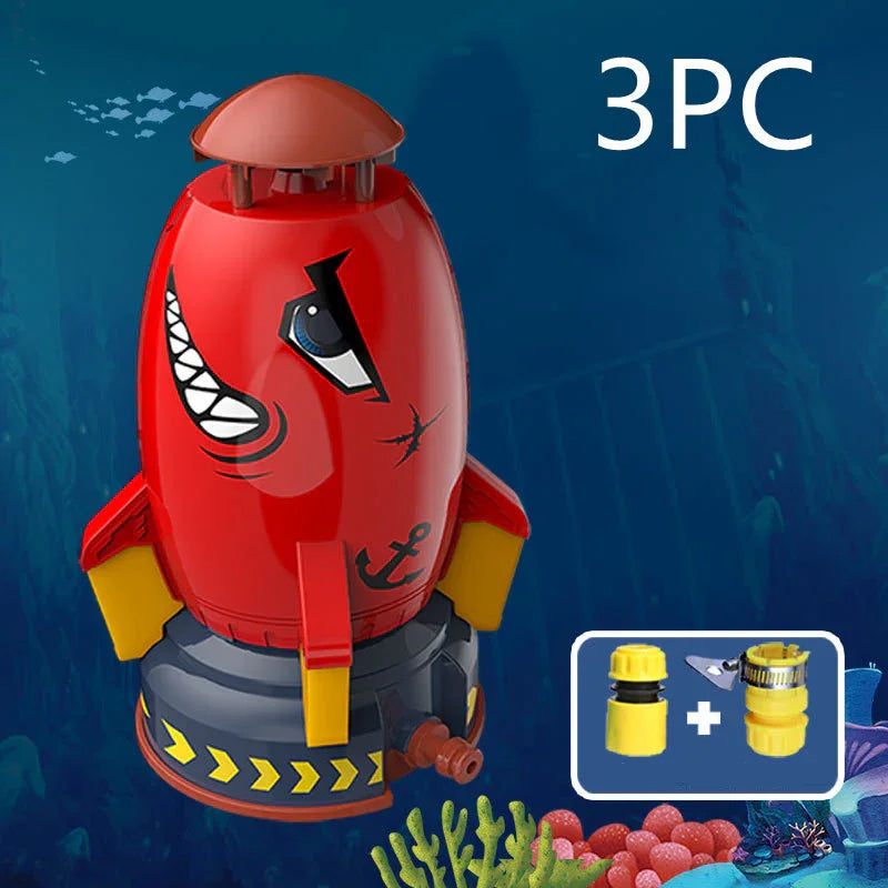 Red plastic rocket-shaped water sprinkler with cartoon face and yellow fins, underwater background