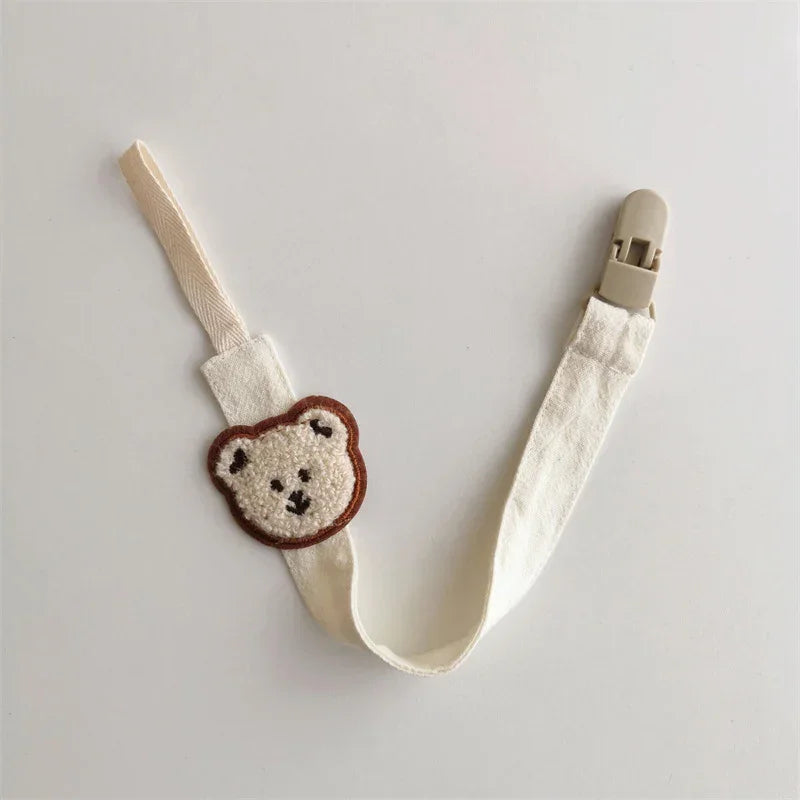 Cream fabric strap with teddy bear patch and beige clip, soft accessory for kids.
