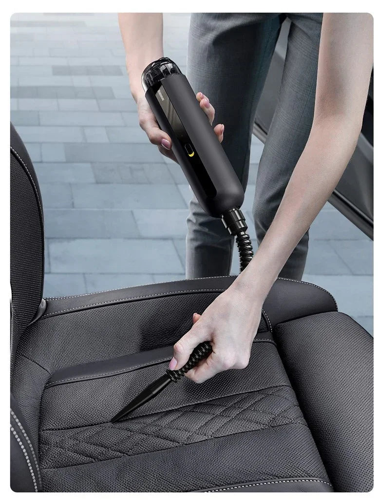 Person using a black handheld vacuum on a textured black car seat