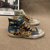 High top denim sneakers with distressed details, bronze studs, graffiti print, and gold laces