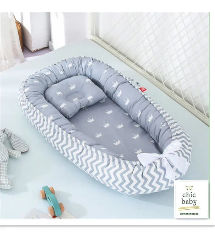 Gray padded baby nest bed with white crown print, soft cotton material, chevron edge, cozy fit.