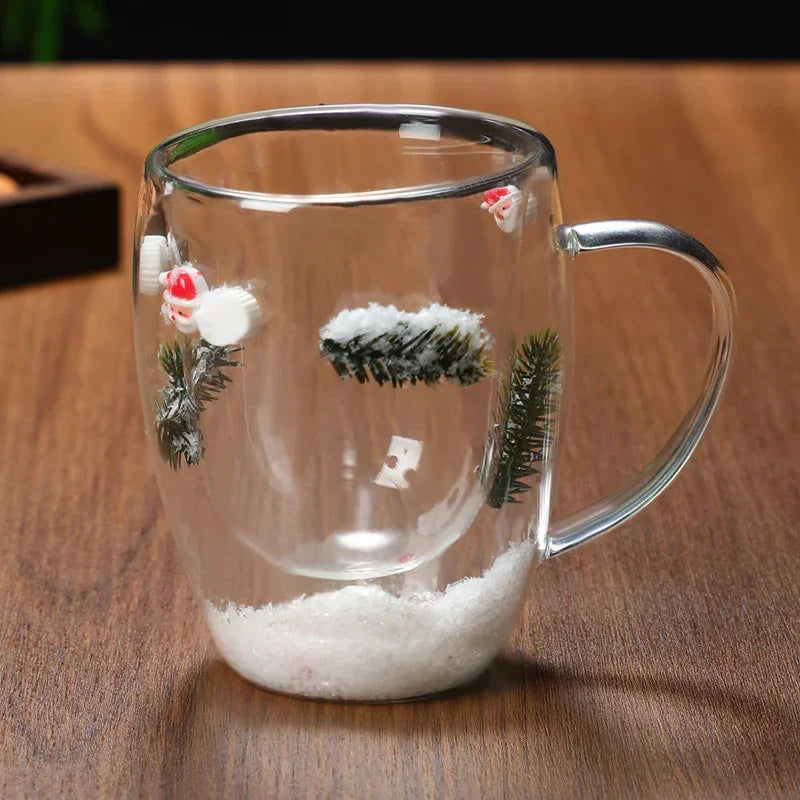 Clear glass mug with winter-themed decorations, snow effect, pine branches, and Santa figures