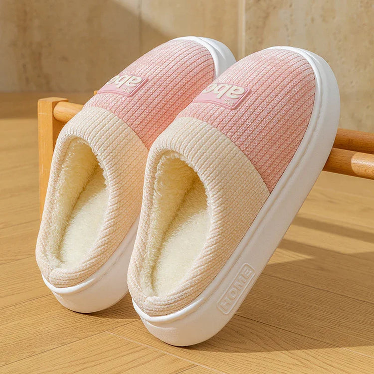 Pink and cream slip-on indoor slippers with ribbed fabric and plush lining on a wooden floor