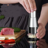 Hands using a stainless steel garlic chopper with chopped garlic in a kitchen setting