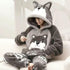 Person wearing grey plush wolf pajama set with hood, animal ears, and relaxed fit on sofa