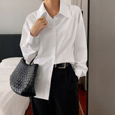 Woman wearing oversized white button-up shirt, black high-waisted trousers, and woven black bag