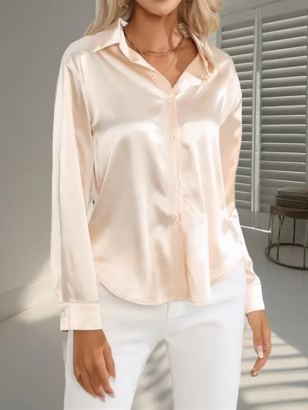 Woman wearing a long sleeve cream satin blouse with white pants, relaxed fit, modern style.