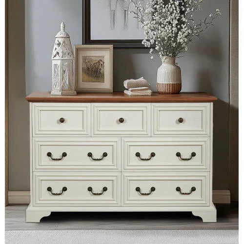 Cream wood dresser with six drawers, bronze handles, and brown wooden top in a modern room.