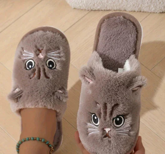 Gray plush cat face slippers with embroidered details on wooden floor, cozy fit