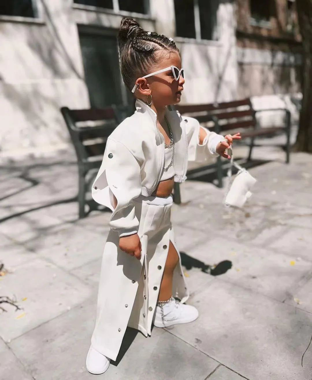 Child wearing a white streetwear set with matching jacket, skirt, and sneakers, outdoors