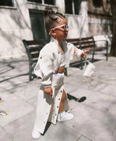 Child wearing a white streetwear set with matching jacket, skirt, and sneakers, outdoors