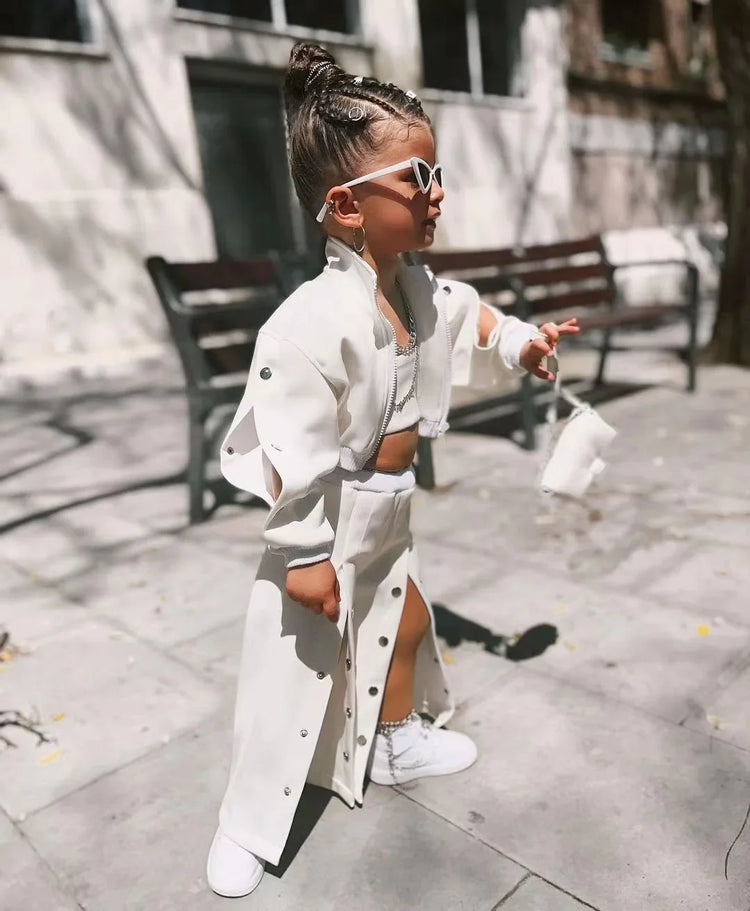 Child wearing a white streetwear set with matching jacket, skirt, and sneakers, outdoors