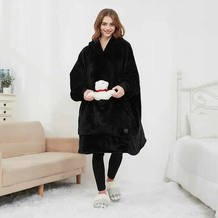 Woman wearing oversized black fleece hoodie blanket, black leggings, and slippers in cozy bedroom