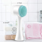 White and turquoise silicone facial cleansing brush with ergonomic handle, shown in bathroom setting.