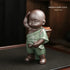 Ceramic figurine of a child in green robe with brown boots, carrying a basket, glossy finish, standing pose.