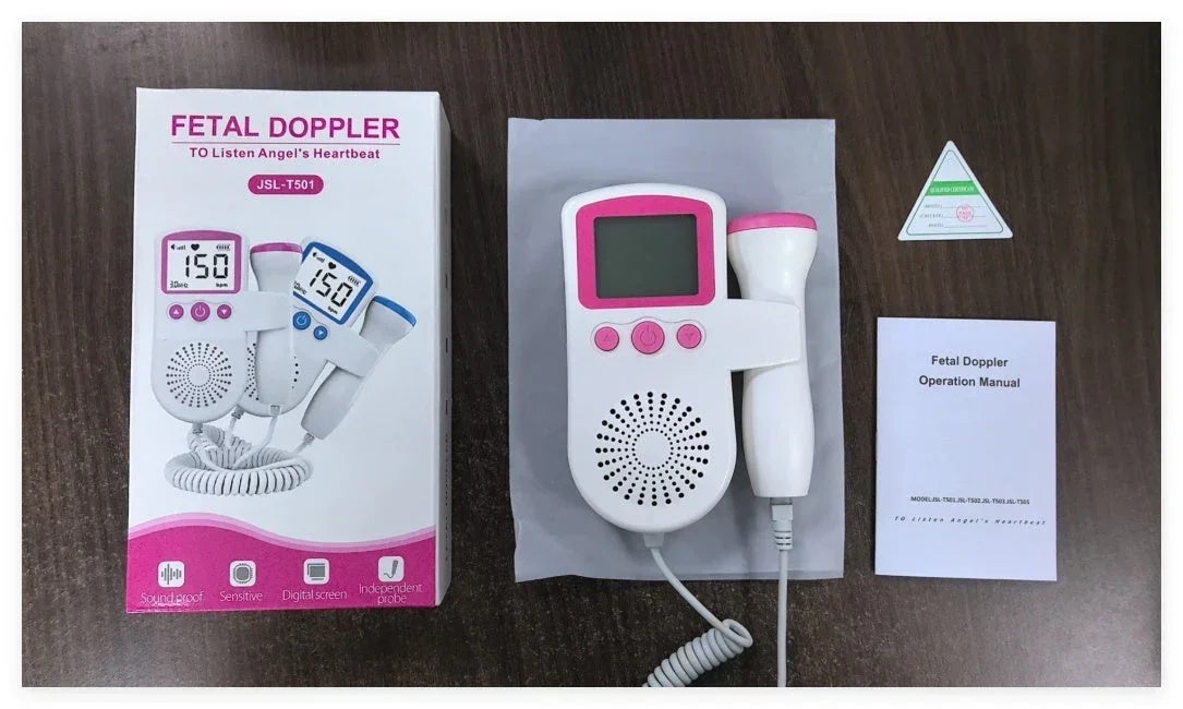 No clothing visible; electronic fetal doppler device with pink and white body, digital display, and probe on a dark surface next to packaging and user manual.