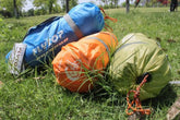Colorful nylon drawstring bags with outdoor camping gear lying on grass in sunlight