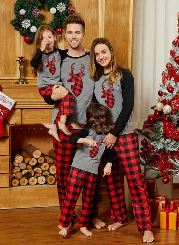 Family wearing matching plaid Christmas pajamas with red and black check pants and gray reindeer tops