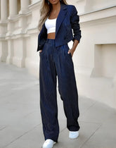 Woman wearing navy pinstripe oversized blazer and wide-leg pants with a white crop top and sneakers