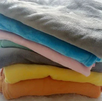 Stack of soft fleece blankets in gray, blue, pink, yellow, and orange, folded neatly
