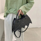Green striped oversized top with loose white pants, holding black bat-shaped handbag with web detail.