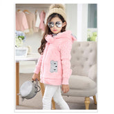 Girl in pink faux fur hooded jacket with bear patch, cable-knit sleeves, and white pants