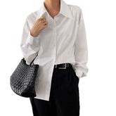 Woman wearing oversized white button-up shirt with black trousers and woven black bag
