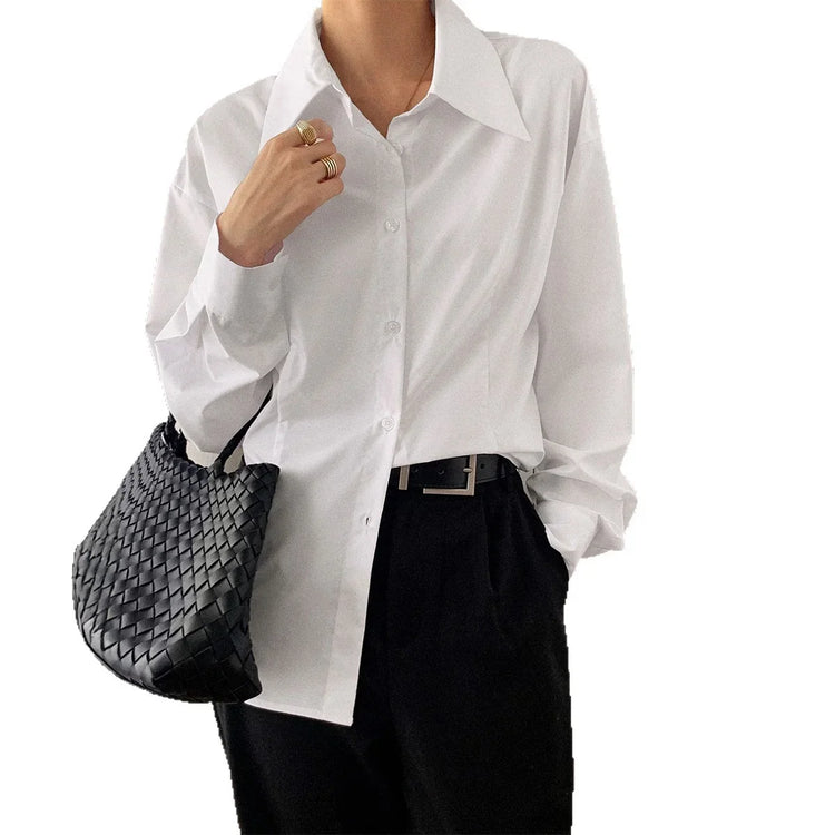 Woman wearing oversized white button-up shirt with black trousers and woven black bag