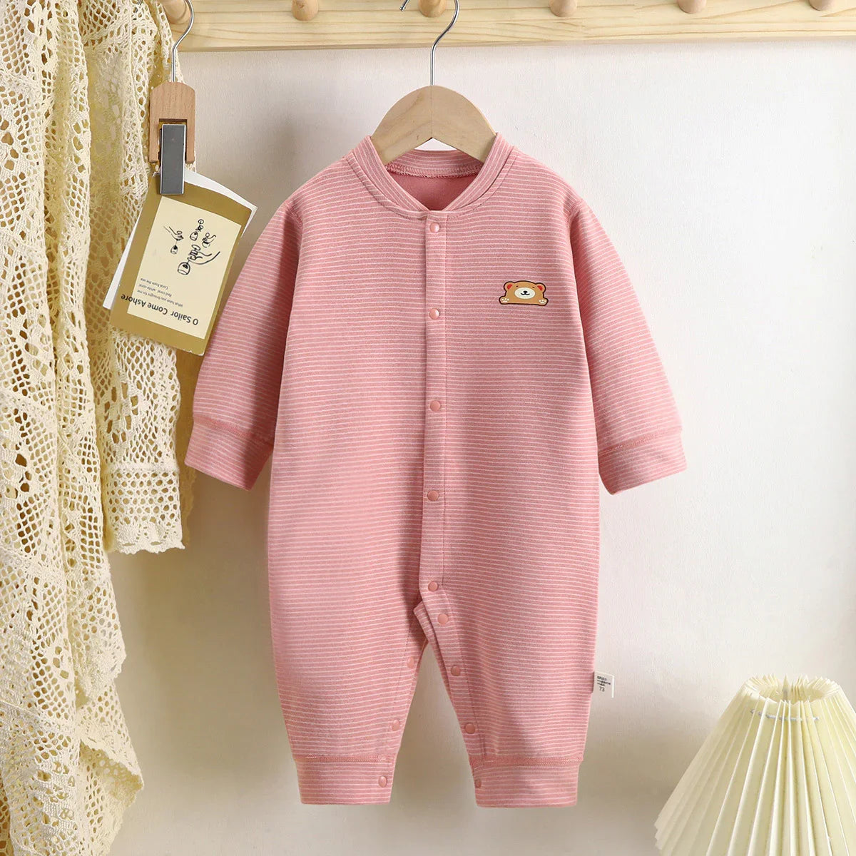 Pink striped baby romper with long sleeves, front snaps, and bear patch, soft cotton fabric
