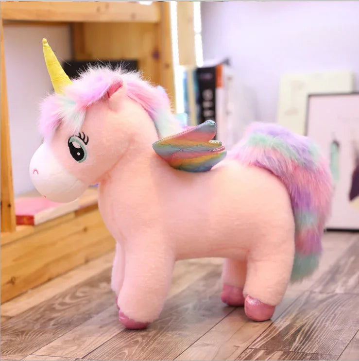 Soft pastel plush unicorn toy with rainbow wings and fluffy mane, pink color, standing indoors