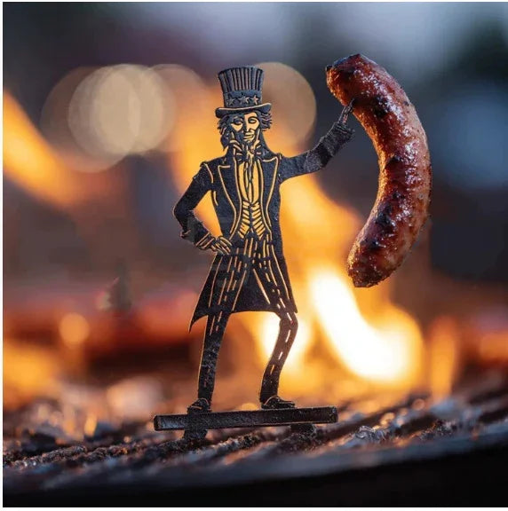 Metal cutout figure in vintage suit, holding sausage over campfire flames