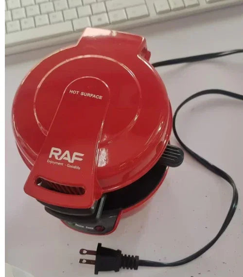 Red electric waffle maker with a closed lid, non-stick surface, and power cord on a white counter.