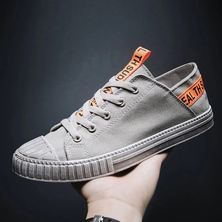 Gray canvas low-top sneaker with rubber sole and orange accent tags, casual streetwear style