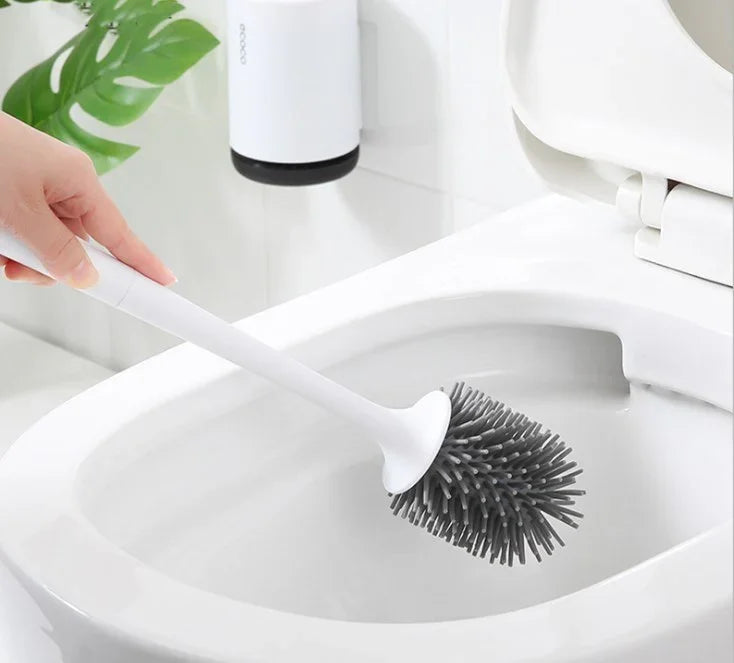 Hand using a gray silicone toilet brush with white handle to clean a toilet bowl