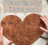 Heart-shaped wooden puzzle with engraved love messages, held by two hands on a neutral surface
