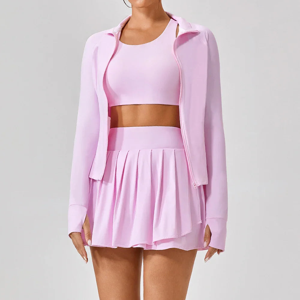 Woman in light pink pleated tennis skirt, crop top, and zip-up jacket set, sporty fit