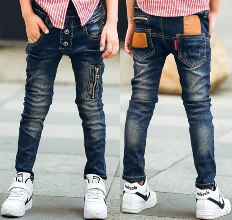 Kids' slim fit blue denim jeans with button fly, front zipper detail, and tan pocket accent