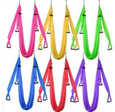 Colorful nylon aerial yoga hammocks with handles, hanging in rows for fitness and stretching.