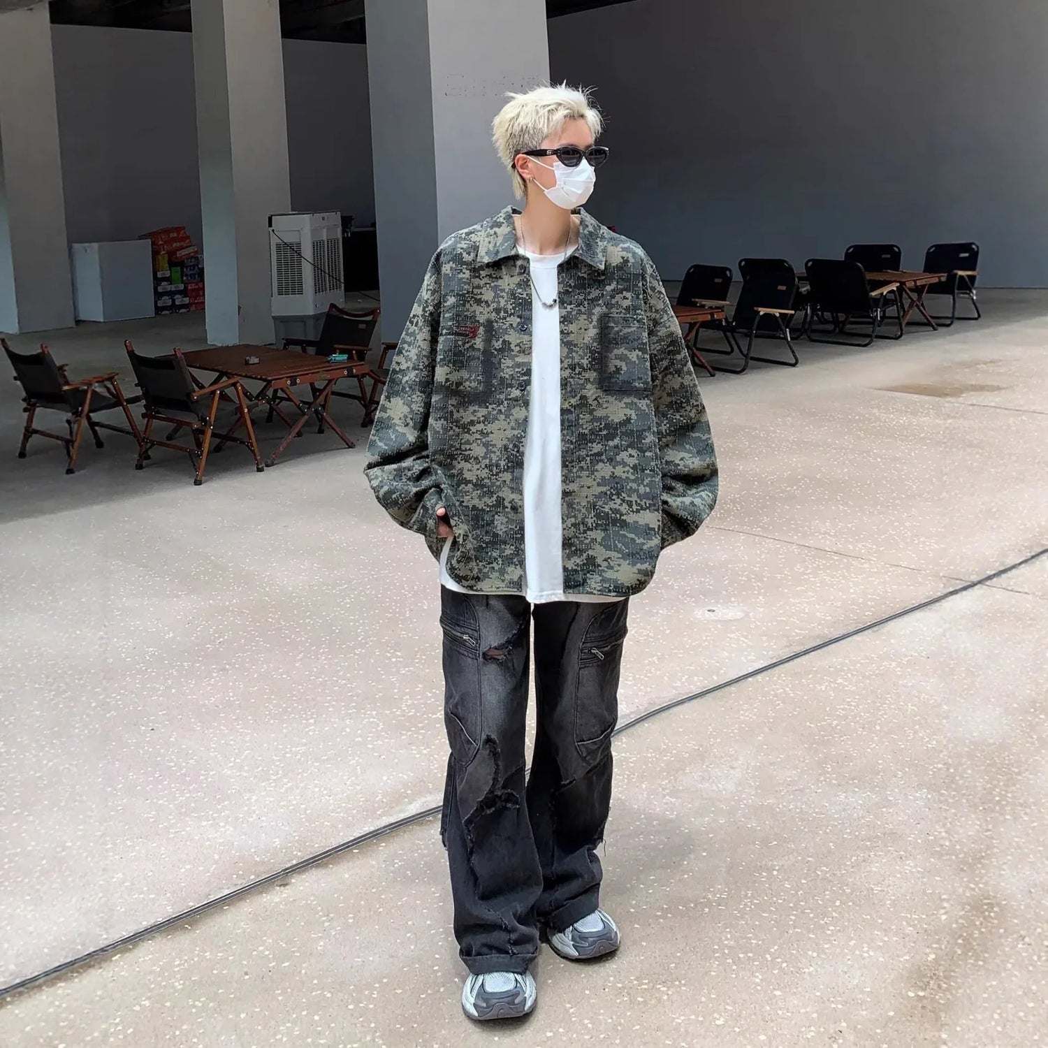 Person in oversized camouflage jacket, loose white T-shirt, distressed black jeans, and sneakers