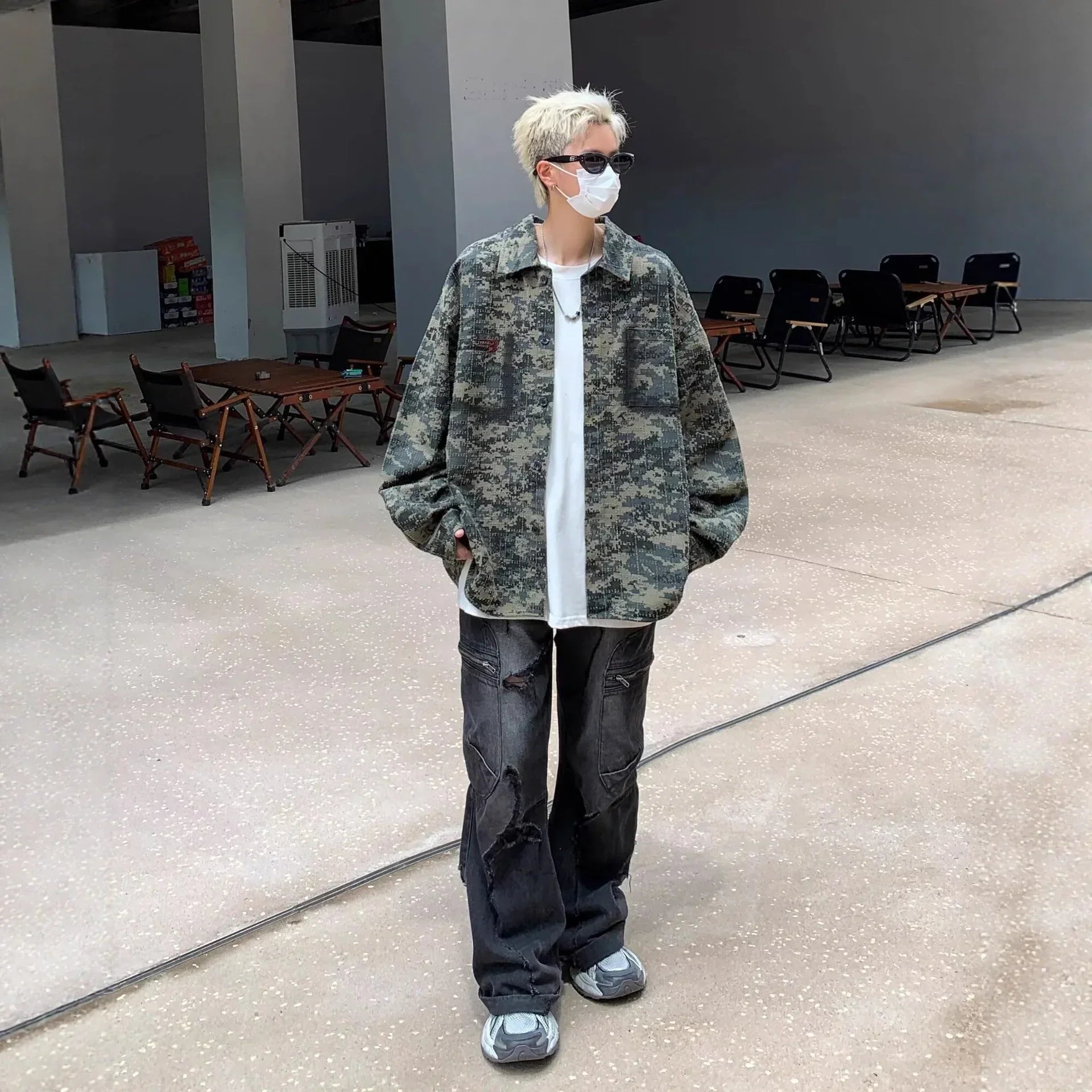 Person in oversized camouflage jacket, loose white T-shirt, distressed black jeans, and sneakers