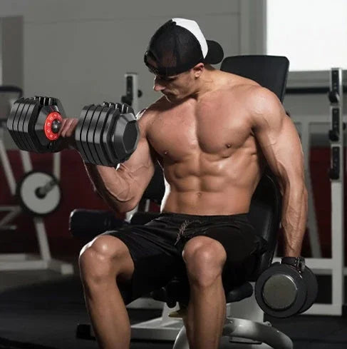 Man in black athletic shorts and snapback hat lifting adjustable dumbbells in gym setting