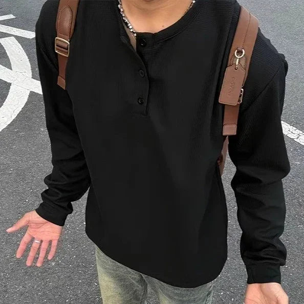 Man wearing a black long sleeve henley shirt with a relaxed fit and brown suspenders outdoors.