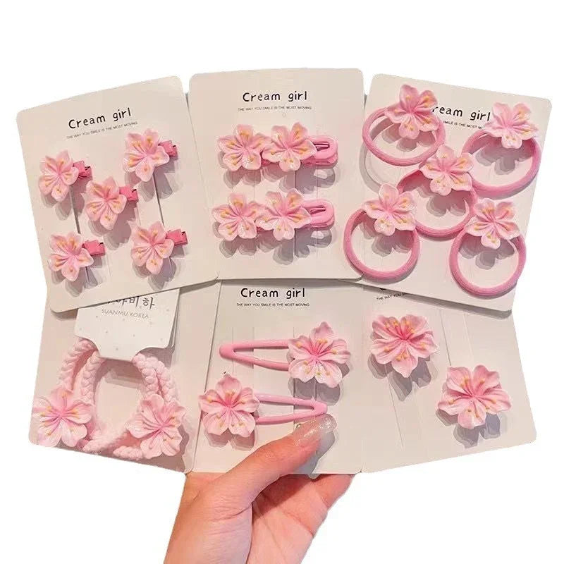 Assorted pink hair clips and elastic bands with decorative flower accents, soft pastel style.
