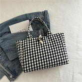Black and white gingham tote bag with rope closure on denim jacket, casual streetwear style