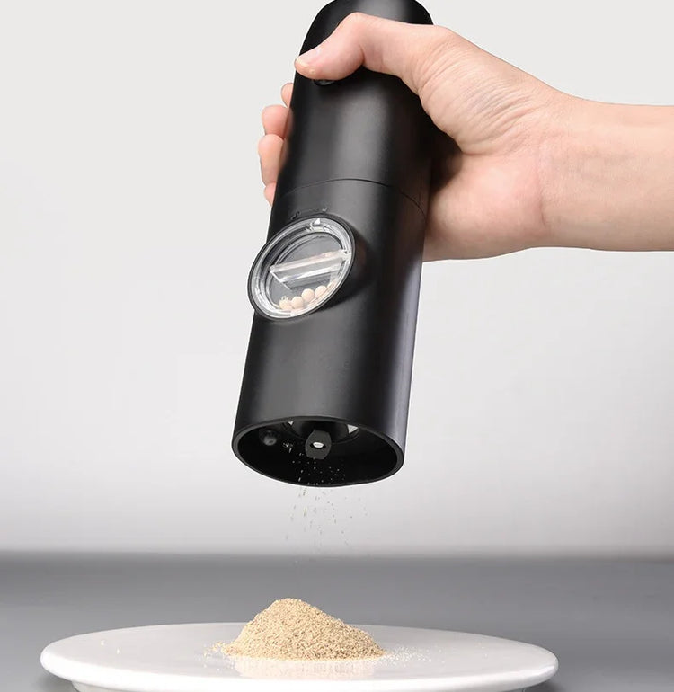 Hand using sleek black electric pepper grinder to season food on white plate